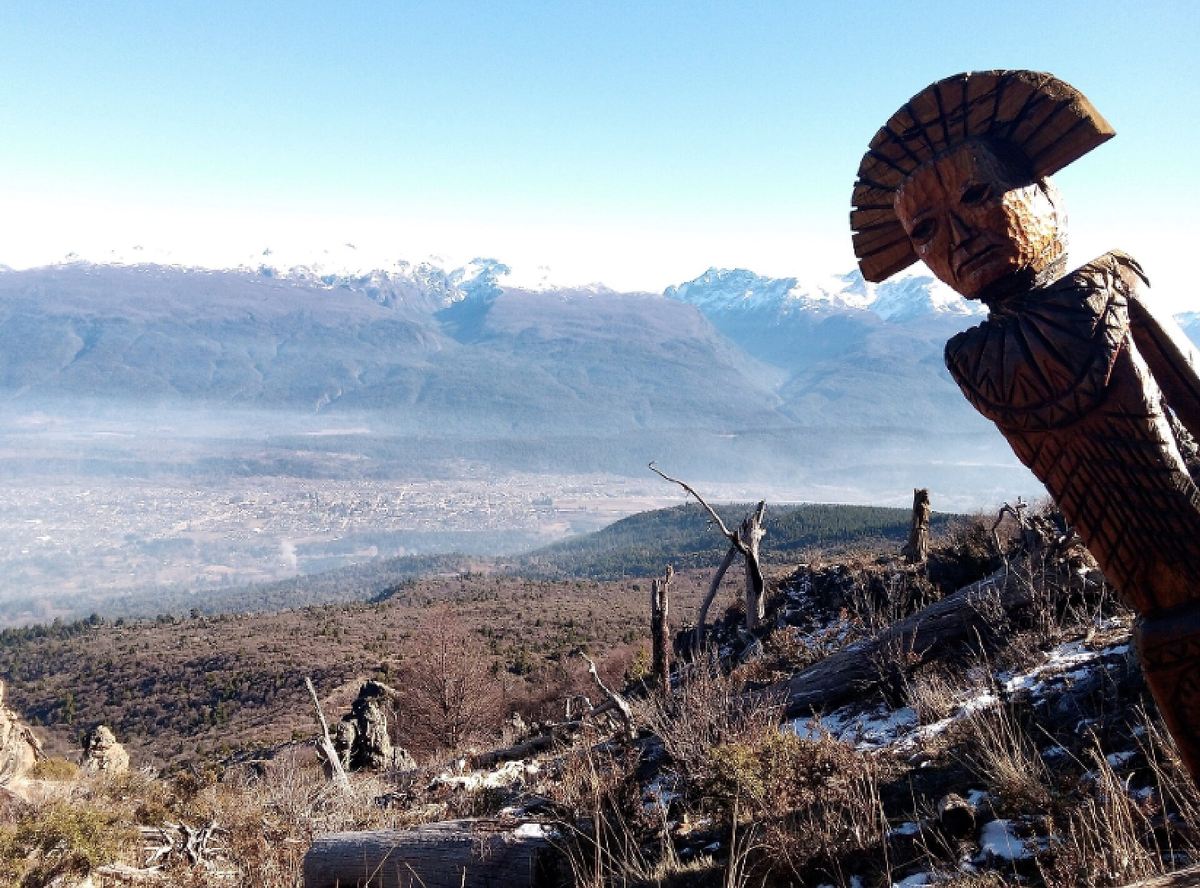 Una escultura del Bosque Tallado con el cordón nevado de fondo, en agosto.